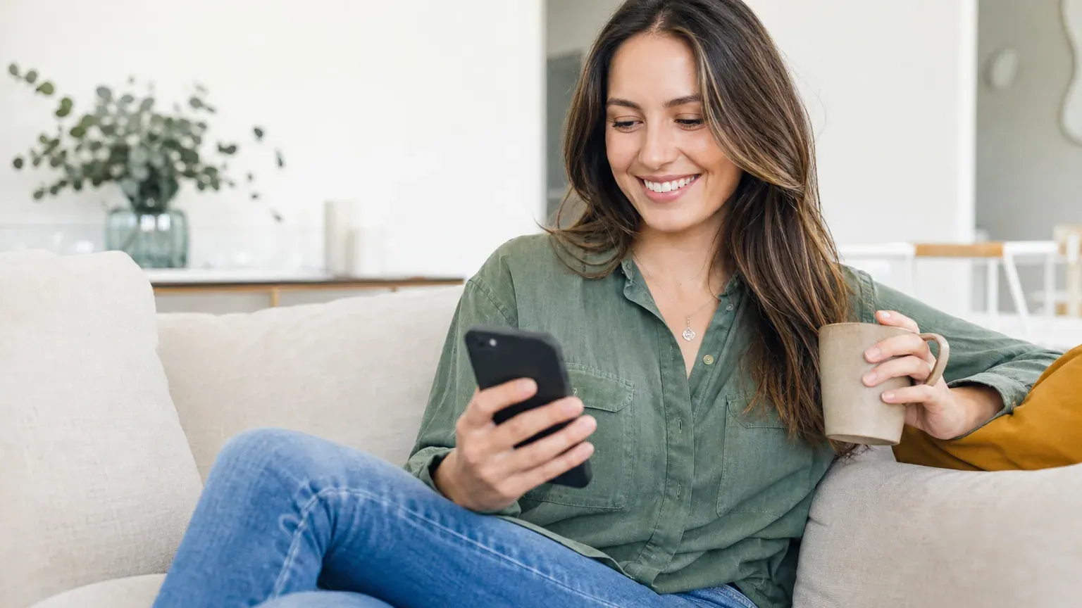 Personne souriante consultant son smartphone en buvant un café dans un salon lumineux