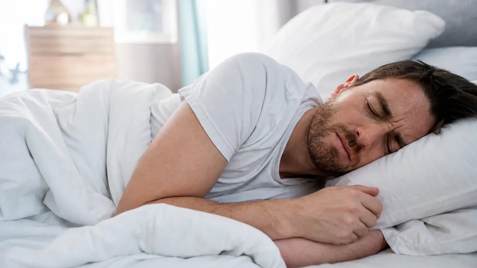 Personne endormie dans un lit, la mâchoire crispée, illustration du bruxisme nocturne
