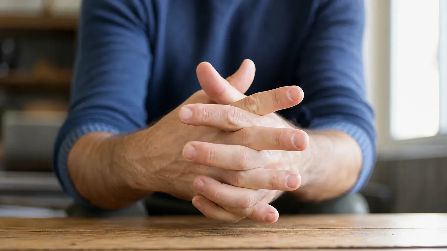 Mains aux doigts entrelacés posées sur une table en bois, prêtes à faire craquer les articulations